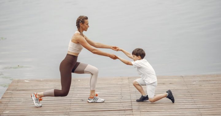 A woman and a boy exercise together on a wooden deck by the lake, promoting healthy lifestyle.