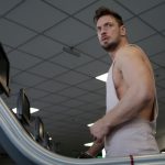 Low angle of muscular adult male athlete in sportswear during training on running machine in modern spacious fitness center while looking away