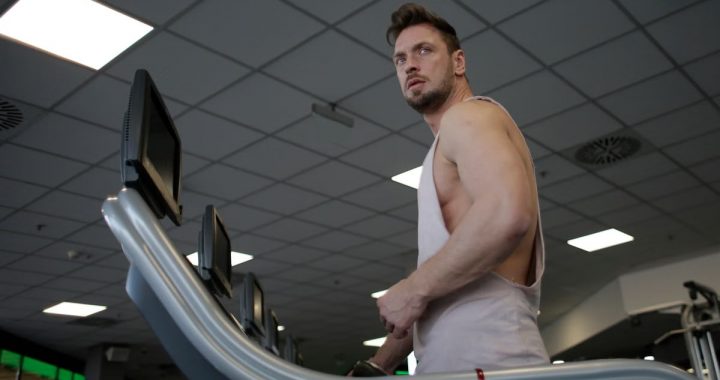 Low angle of muscular adult male athlete in sportswear during training on running machine in modern spacious fitness center while looking away