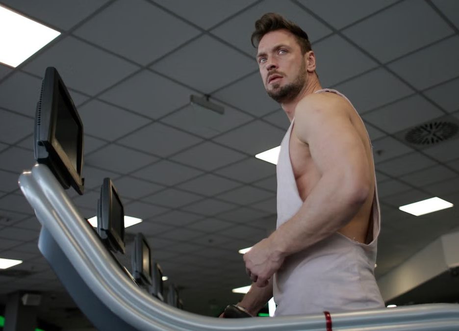 Low angle of muscular adult male athlete in sportswear during training on running machine in modern spacious fitness center while looking away